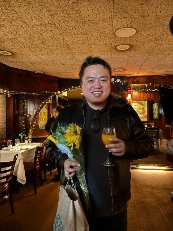 swyx smiling with a bouquet of flowers and a drink